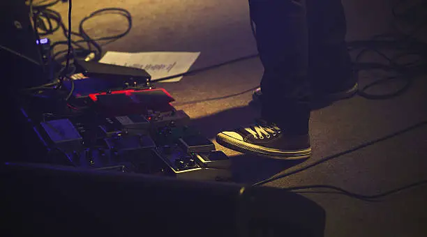 Electric guitar player on a stage with set of distortion effect pedals under his foot. Selective focus, vintage tonal correction filter effect, old style