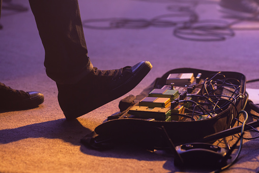 Electric bass guitar player on a stage with set of distortion effect pedals under his foot. Selective focus