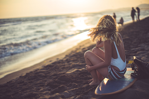 Woman sitting on the surfboard in time of sunset and touching her blonde hair