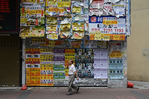 Kowloon, Hong Kong - September 19, 2016: Man is walking on a sidewalk in Mong Kok district passing by a wall full of crinkle advertisements, Kowloon Peninsula. With its extremely high population density this district in Hong Kong was described as the busiest district in the world.