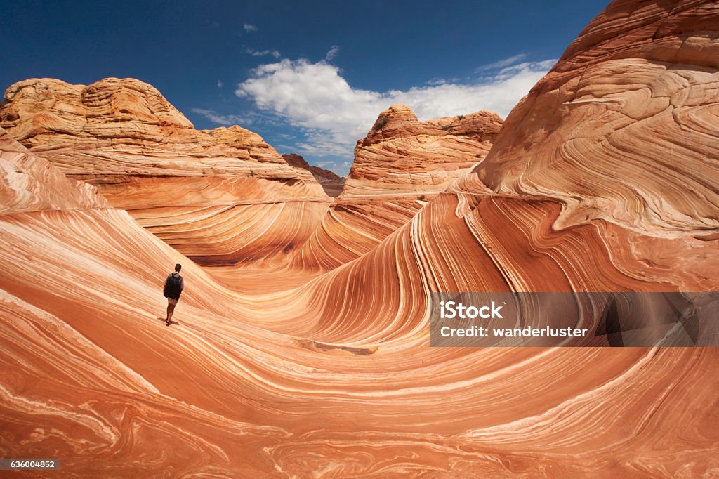 Lone hiker at Arizona's Wave Adult male tourist hikes across the striated sandstone rock formations known as the Wave located within the Paria Canyon-Vermilion Cliffs Wilderness, Page, Arizona, US, North America USA Stock Photo