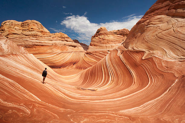Lone hiker at Arizona's Wave Adult male tourist hikes across the striated sandstone rock formations known as the Wave located within the Paria Canyon-Vermilion Cliffs Wilderness, Page, Arizona, US, North America majestic stock pictures, royalty-free photos & images