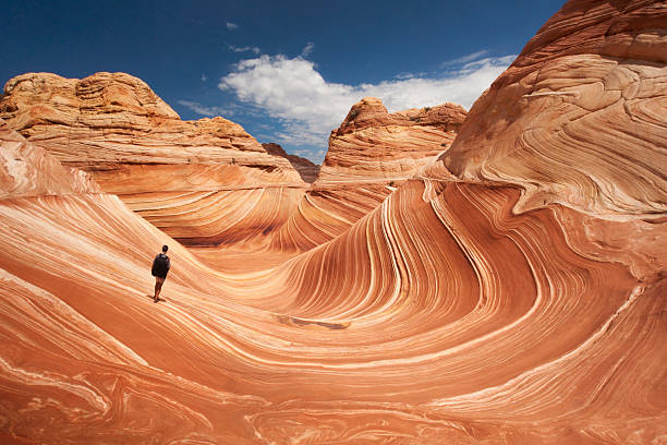 Lone hiker at Arizona's Wave Adult male tourist hikes across the striated sandstone rock formations known as the Wave located within the Paria Canyon-Vermilion Cliffs Wilderness, Page, Arizona, US, North America geology stock pictures, royalty-free photos & images