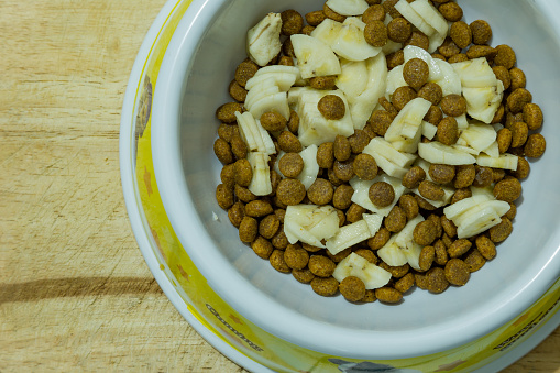 Dog food mixed with banana and milk in a bowl on wooden background
