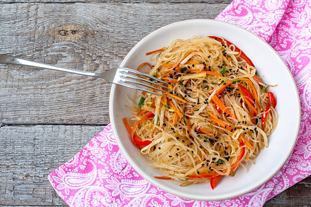 Rice noodles with vegetable stir fry on the ceramic bowl on dark wooden backgroundRice noodles with vegetable stir fry on the ceramic bowl on dark wooden background