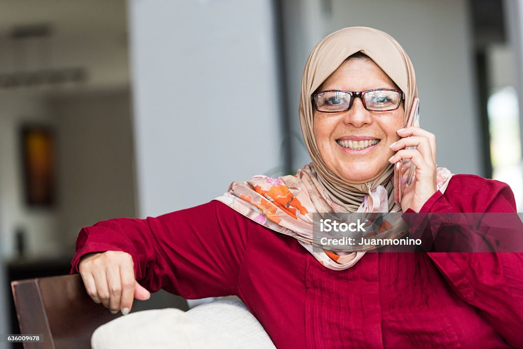 Smiling middle eastern woman close up picture of a smiling mature middle eastern muslim woman wearing a veil posing at her home using her smart phone Using Phone Stock Photo