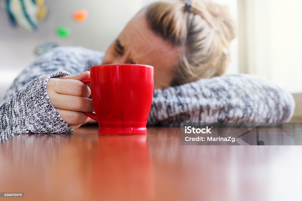 Depressed woman with a cup of coffee in hand Depressed woman laying on a desk with a cup of coffee in hand Coffee - Drink Stock Photo