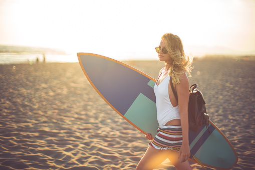 Woman with a surfing board on the beach at sunset