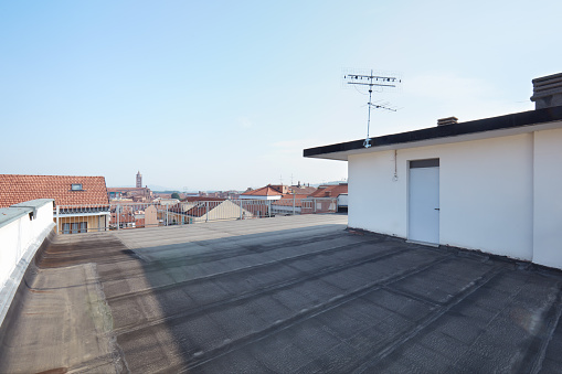 Top of a building with one window and blue sky above.