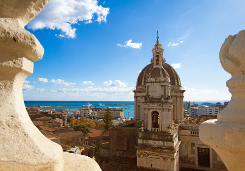 Catania, Sicily: Beautiful old town panorama with the cupola of the 18th-century Duomo di Sant'Agata and a turquoise sea framed (in the foreground) by two baroque architectural flourishes.