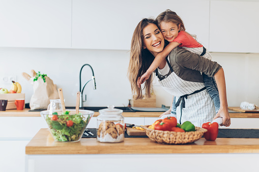 Beautiful mother and daughter having fun piggy-back ride in the kitchen.