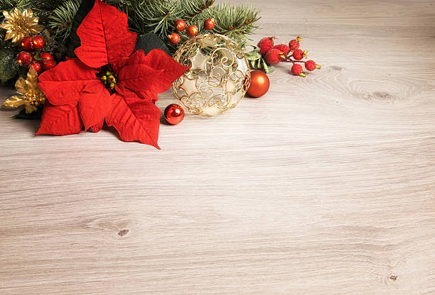 Wooden background with poinsettia, decorated Christmas tree twigs in one corner, text space