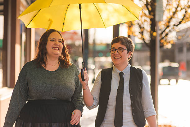 Homosexual couple spending time together and laughing in the city A lesbian couple are  walking out in the city together with an umbrella while laughing transgender person photos stock pictures, royalty-free photos & images