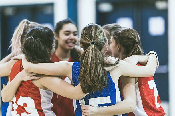 Group of female high school basketball players encouraging one another Group of female high school basketball players encouraging one another by hugging each other in a circle before a competative basketball game secondary school stock pictures, royalty-free photos & images