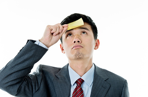 Tired asian businessman with yellow sticky note on forehead