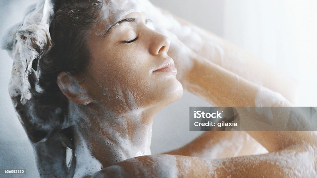 Pleasure of a shower. Closeup side view of attractive mid 20's woman taking a shower in her bathroom after a long exhausting day at work or college. She's gently washing her hair and skin. Shampoo Stock Photo