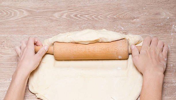 istock Rolling dough with a wooden roller on the table. 636052710