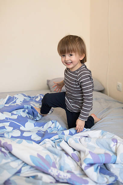 istock blond boy jumping on bed playing real interior, soft focus 636052900