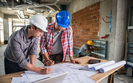 Architect and construction worker reviewing blueprint together.