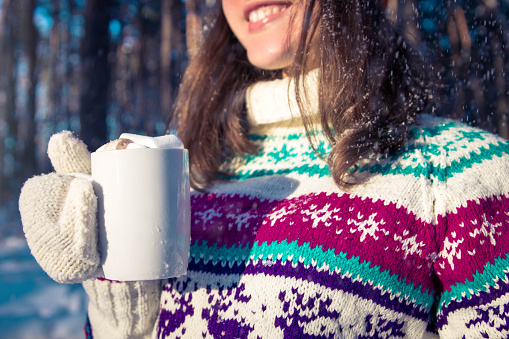 Young woman holds cup of coffee with marshmallow in winter forest