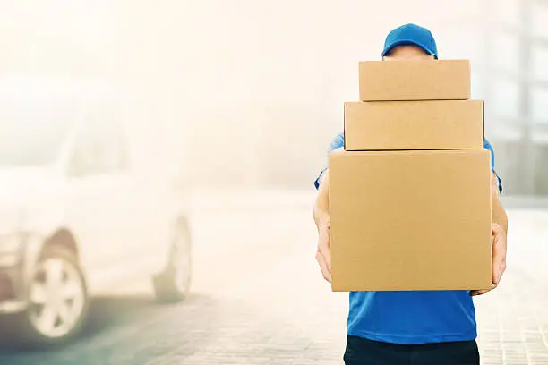 Photo of delivery man holding pile of cardboard boxes in front