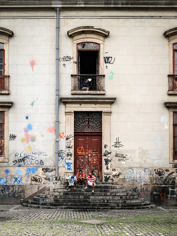 Rio De Janeiro, Brazil - 11 July 2014: A contrast of architecture and circumstance as a group of Brazilian men sit passing time on the stairs to a grand colonial era building defaced by graffiti and time.