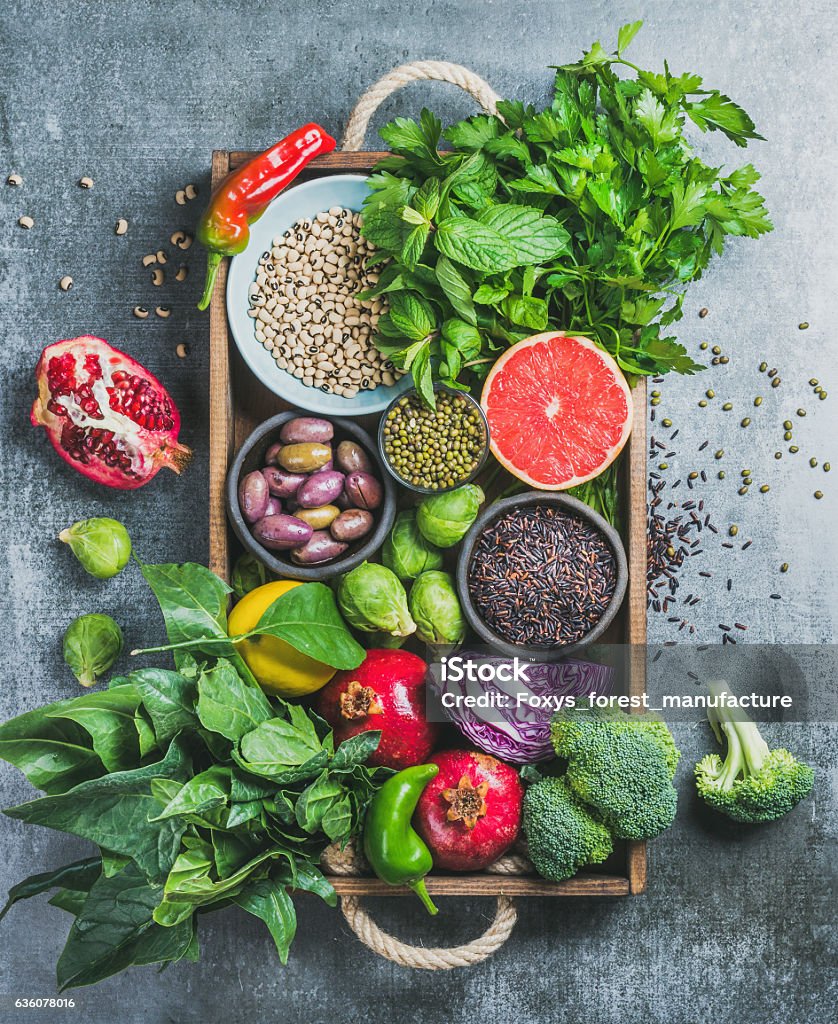 Healthy food ingredients in wooden box over grey background Vegetables, fruit, seeds, cereals, beans, spices, superfoods, herbs, condiment in wooden box for vegan, gluten free, allergy-friendly, clean eating or raw diet. Grey concrete background and top view Vegetable Stock Photo