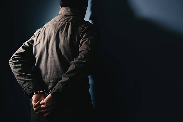 istock Arrested male criminal with handcuffs facing prison wall 636083376