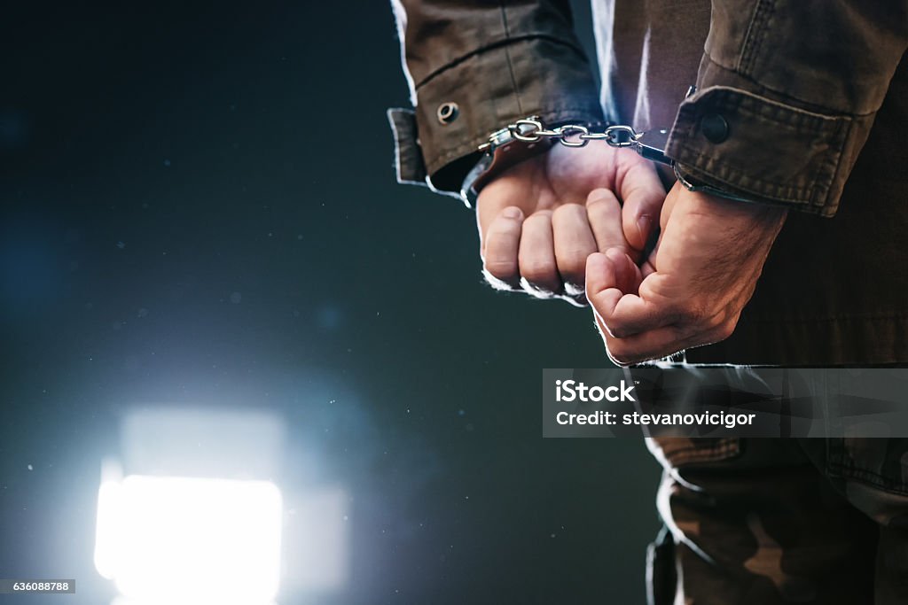 Handcuffed soldier Handcuffed soldier, arrested male army officer in dark prison cell Handcuffs Stock Photo