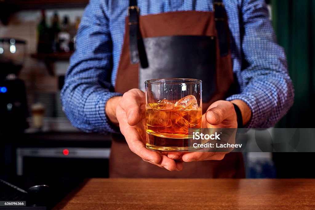 Hands of a bartender at bar restaurant with glass whiskey Hands of a bartender at bar restaurant with glass whiskey drink with ice in his hands closeup Bartender Stock Photo