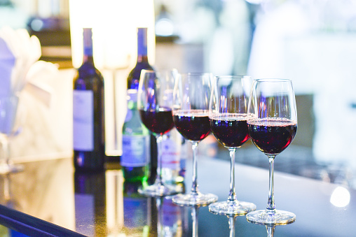Four glasses of red wine with bottle background on counter bar in blue light. select focus and grain image to vintage style