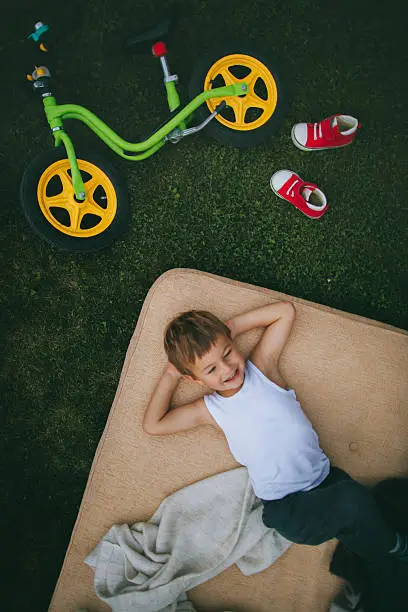 Little boy is resting on the lawn in his backyard after bike ride