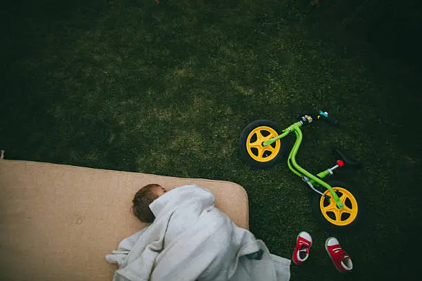 Little boy is resting on the lawn in his backyard after bike ride