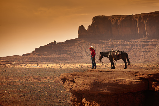 A retro sepia toned portrait of a wild west cowboy on horse back. Photographed in the American southwest, the Monument Valley Tribal Park. in Arizona, USA. Photo in panoramic horizontal format with copy space.