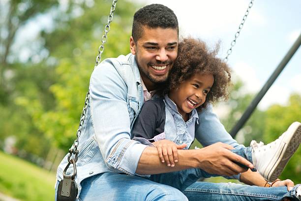 szczęśliwy ojciec i córka. - child swinging playground african descent zdjęcia i obrazy z banku zdjęć