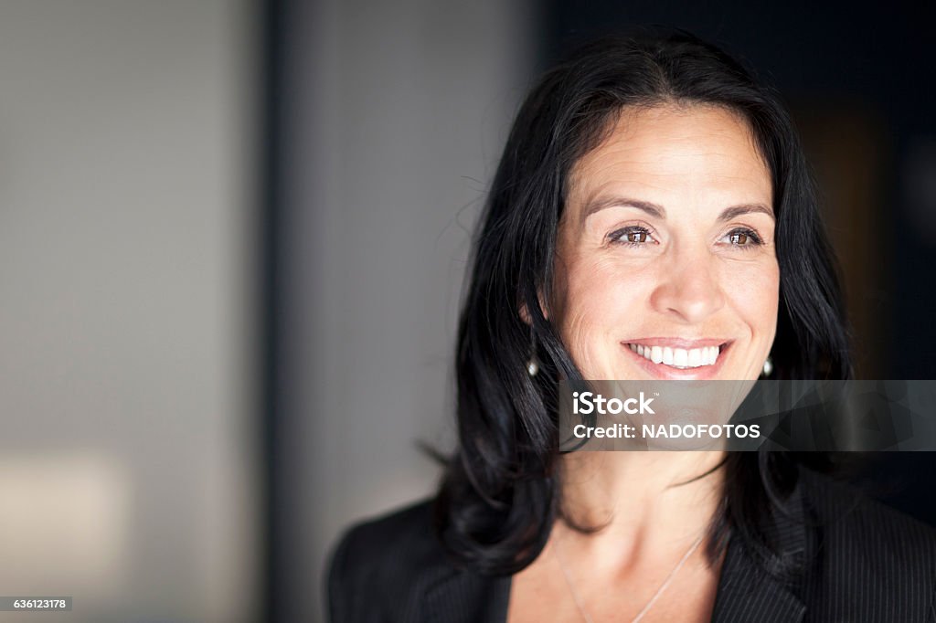 Empresária espanhola madura sorrindo e olhando para o lado. No escritório. - Foto de stock de Cabelo Castanho royalty-free