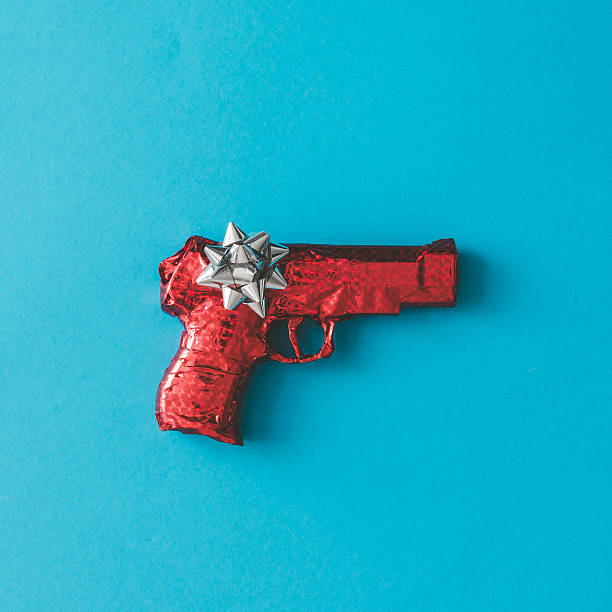 Gun wrapped in red paper with bow on blue background. Flat lay Christmas concept.