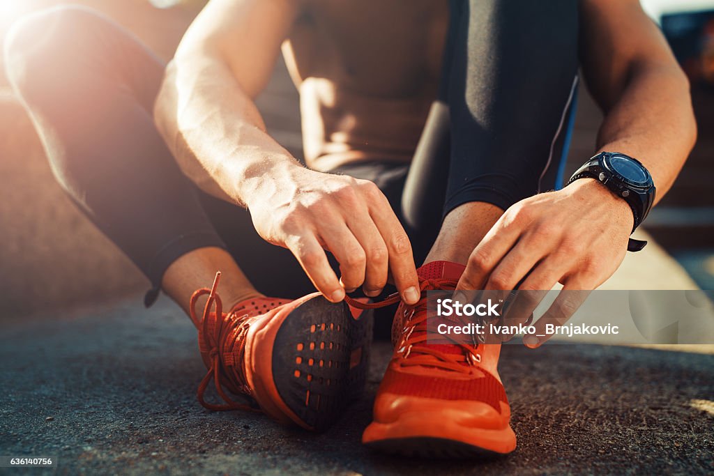 Jogger tying shoe before jogging Young male jogger athlete training and doing workout outdoors in city. Men Stock Photo