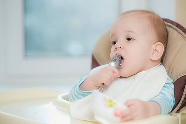 istock baby holding a spoon in his mouth 636145624