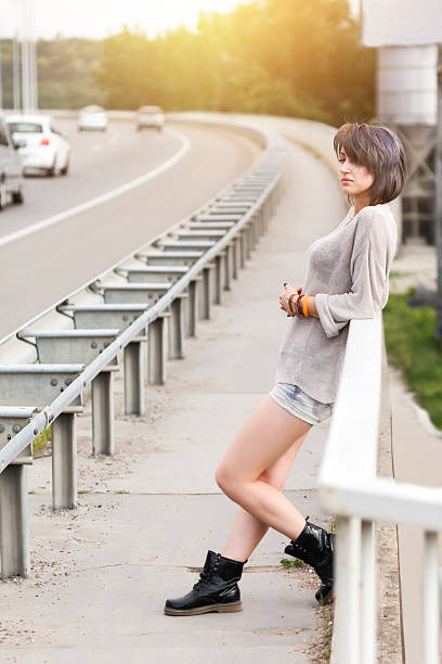 Beautiful girl standing on bridge watching cars go by during sunset