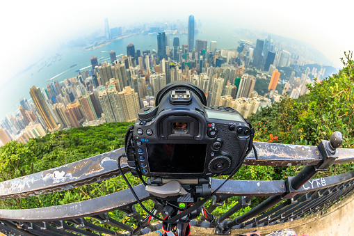 Close up of a professional camera on the tripod while photographing the Victoria Harbour skyline from Lugard Road Lookout at Victoria Peak, the highest mountain in Hong Kong Island. Fisheye lens.