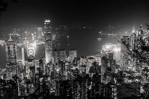 Victoria Harbour skyline by night from Lugard Road Lookout at Victoria Peak, the highest mountain in Hong Kong Island. Panorama of skyscrapers and towers of Hong Kong in black and white.