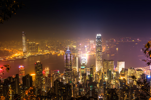 Aerial view of Victoria Harbour skyline by night from Lugard Road Lookout at Victoria Peak, the highest mountain in Hong Kong Island. On backgrond, the landmark skyscrapers with their lights and neon.