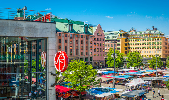 Stockholm, Sweden - July 9, 2016: Cinema, department stores and restaurants overlooking people shopping at the market stalls in the colourful square of Hotorget in the heart of Stockholm, Sweden's vibrant capital city. Composite panoramic image created from five contemporaneous sequential photographs. 