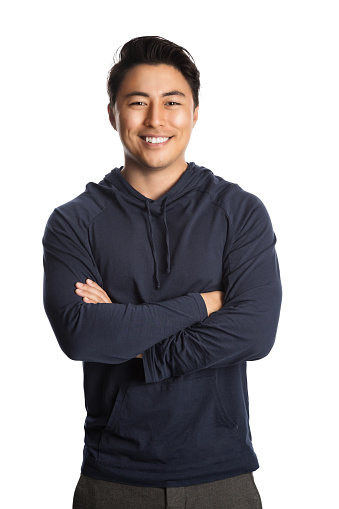 An attractive man in his 20s standing against a white background wearing a blue hood shirt smiling, looking at camera.