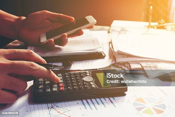 Young Businessman Calculating About Cost And Using Smartphone Se Stock Photo - Download Image Now