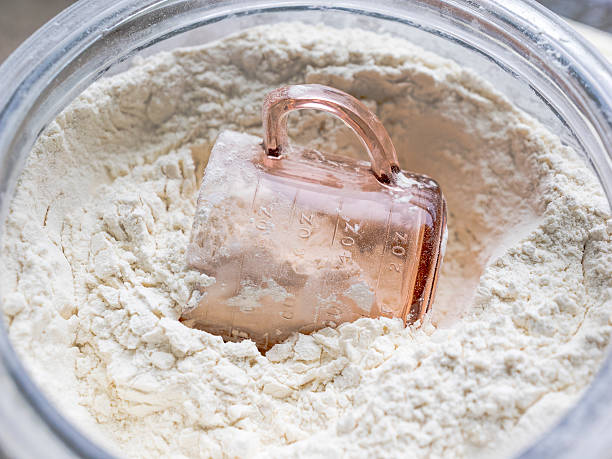 A glass container full of flour with a pink depression glass measuring cup in the flour.