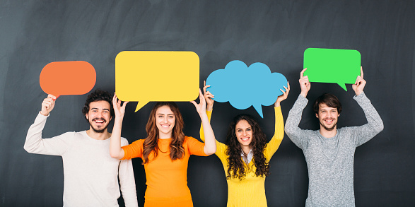 Group of people holding colorful speech bubbles in front of a blackboard.