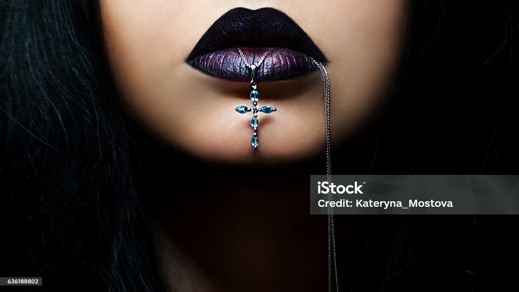 dark hair woman with dark lips with cross in her mouth Portrait of dark hair woman with dark lips with cross in her mouth Goth Stock Photo