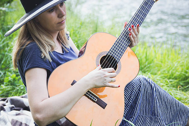 istock young woman sitting on a field and playing guitar 636199308